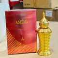 Gold perfume bottle and red packaging with 'AMENA' branding on a wooden surface.
