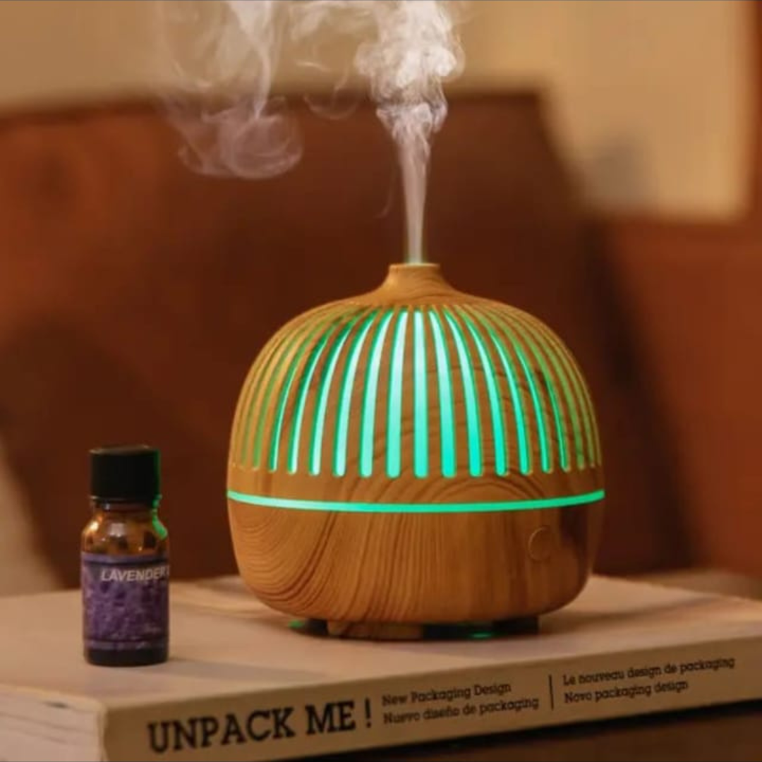Wooden diffuser with green lights and a bottle of essential oil on a surface.